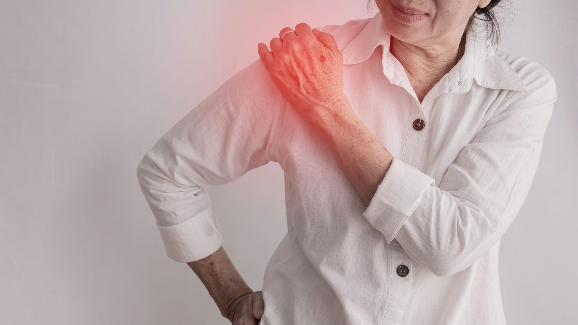 An older woman in a white shirt holds her left shoulder, which is highlighted in red, suggesting pain or discomfort and the possible need for pain management.